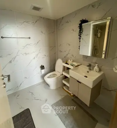 Modern bathroom with sleek fixtures and marble tiles, featuring a compact vanity and mirror cabinet.