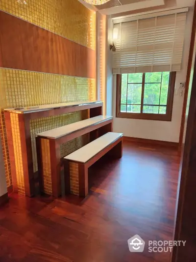 Warm-toned study room with custom built-in desk and bench, hardwood flooring, and a large window inviting natural light.