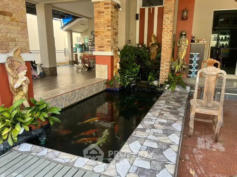 Charming outdoor koi pond with decorative statues and lush greenery in a serene patio setting.