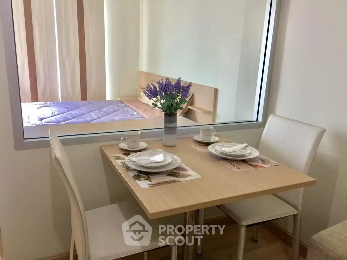 Cozy dining area with table set for two, adjacent to a bedroom with a view through a glass partition.