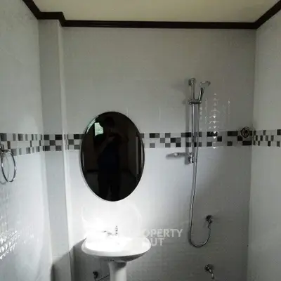 Modern bathroom with oval mirror and shower in tiled interior