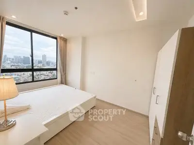 Spacious bedroom with city view, large window, and modern furnishings in a high-rise apartment.