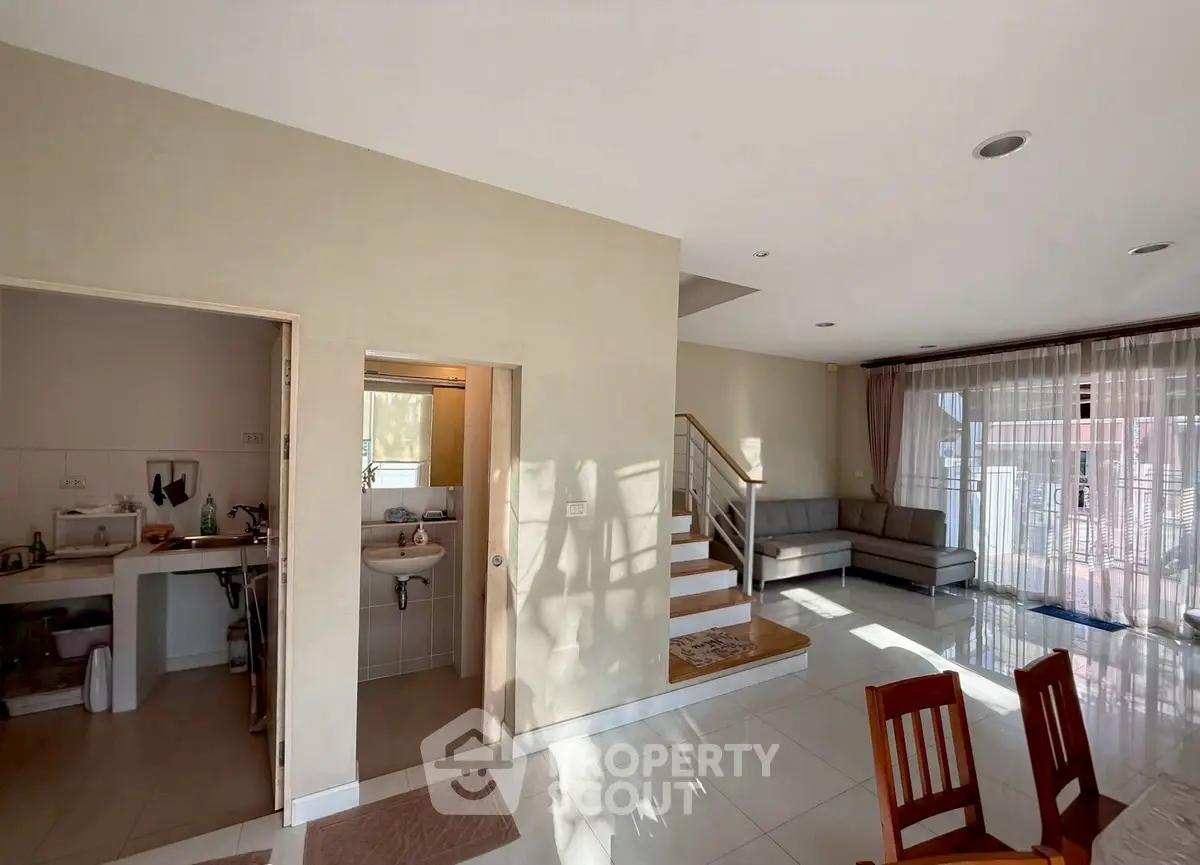 Spacious modern living room with open layout and staircase, featuring large windows and elegant furnishings.