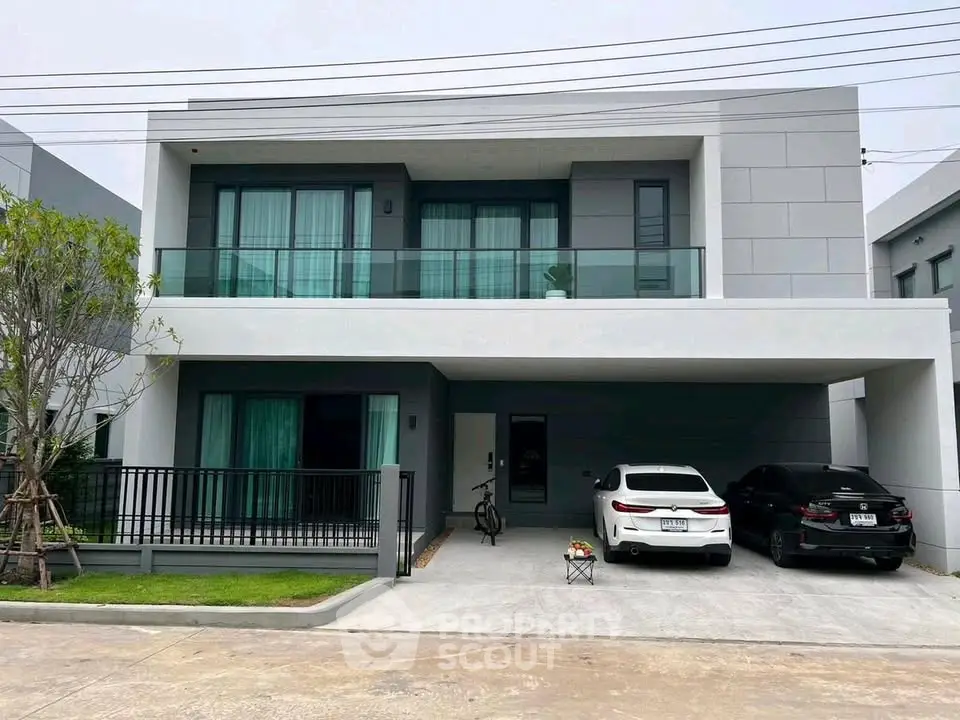 Modern two-story house with spacious driveway and sleek design, featuring large windows and a balcony.