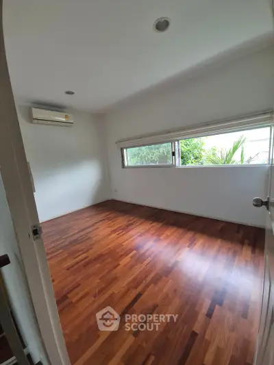 Spacious empty bedroom with wooden flooring and large windows offering natural light.