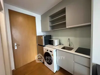 Modern compact kitchen with sleek cabinetry, appliances, and wooden flooring in a stylish apartment.