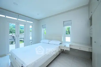 Bright bedroom with large windows and scenic view, featuring modern furniture and neutral decor.