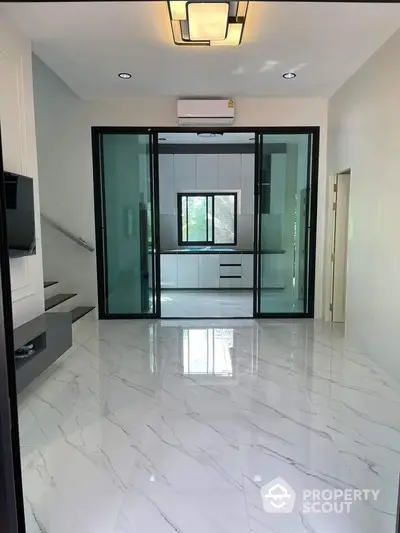 Modern interior with glossy marble floors and glass sliding doors leading to a sleek kitchen.