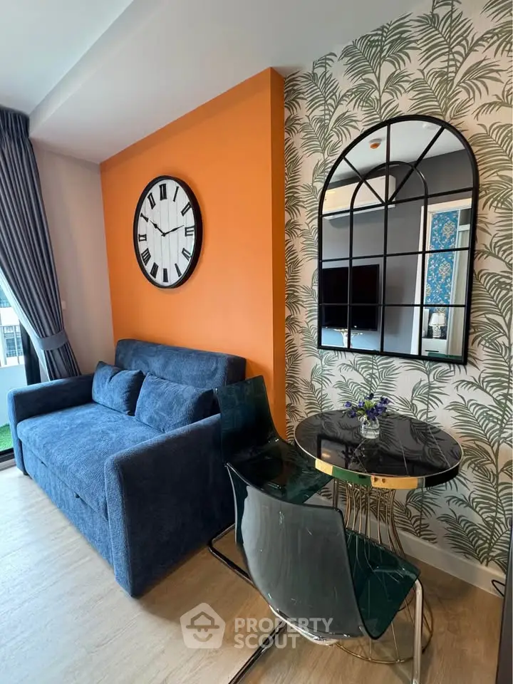Stylish living room with modern decor, featuring a blue sofa, round glass table, and large wall clock.