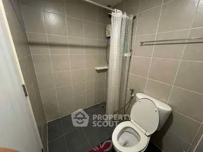 Compact bathroom with shower and toilet in modern tiled design.