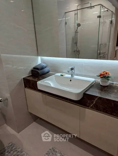Modern bathroom with sleek sink and glass shower enclosure, featuring elegant marble countertop and stylish decor.