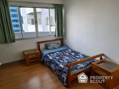 Cozy bedroom with polished wooden flooring, large window allowing ample natural light, and matching wooden bed frame and nightstands.