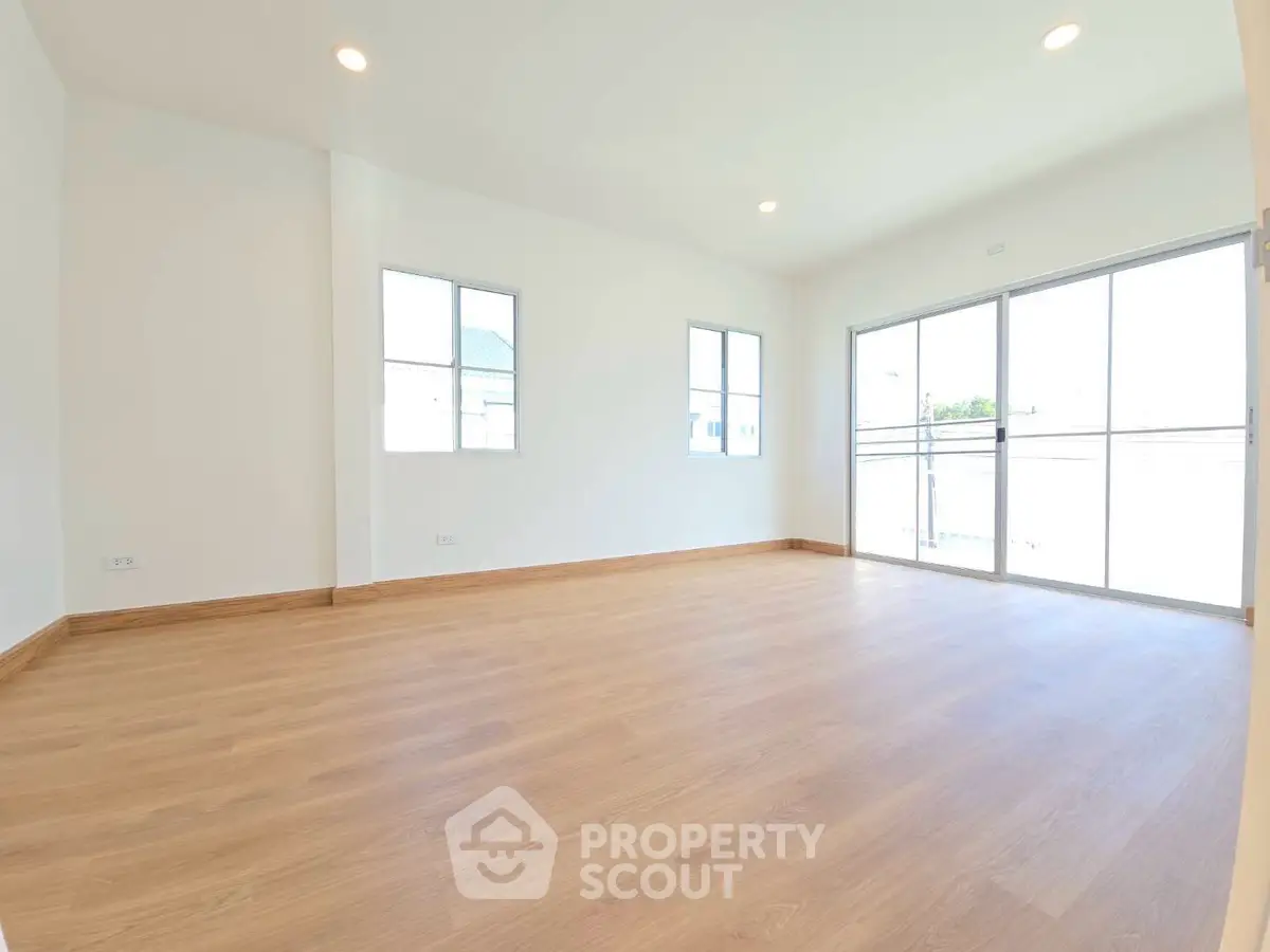 Spacious empty room with wooden flooring and large windows for natural light.