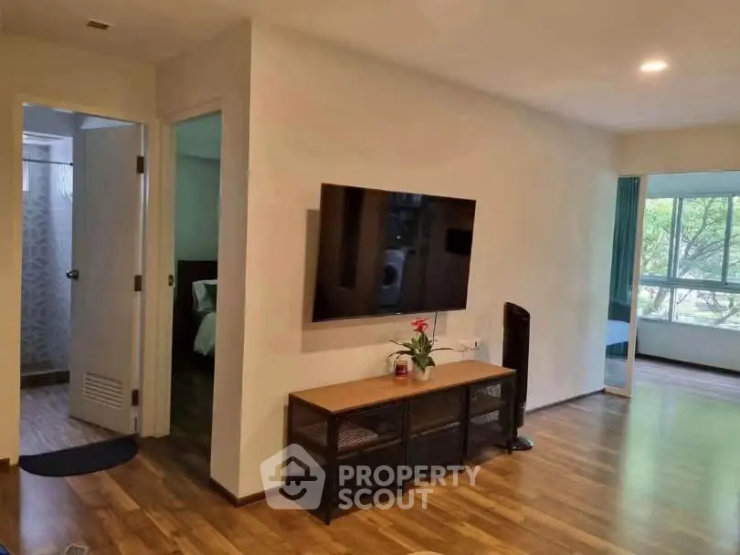 Spacious living room with modern TV setup and wooden flooring, adjacent to a cozy bedroom and bathroom.
