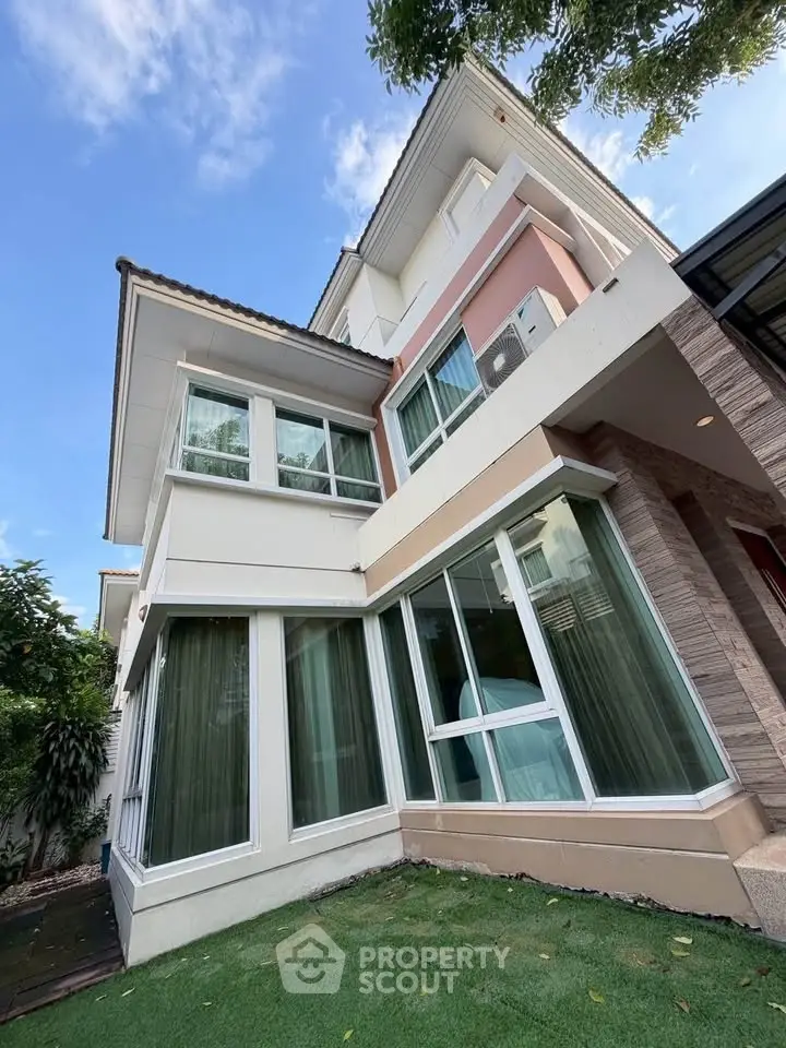 Modern multi-story house with large windows and lush green lawn, showcasing contemporary architecture.