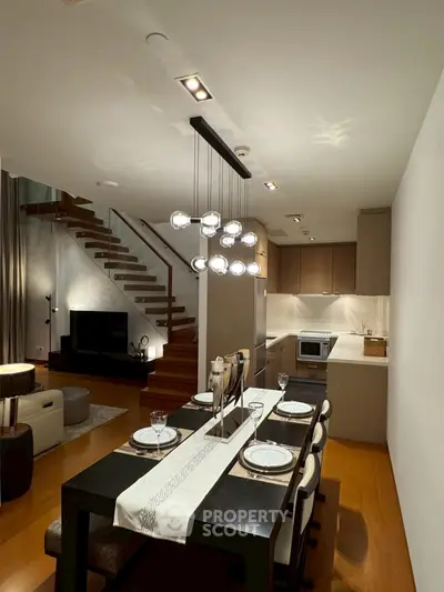 Modern open-plan living and dining area with stylish lighting and wooden staircase.