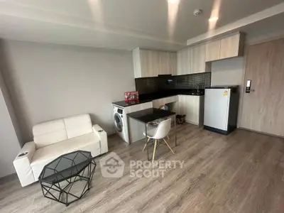Modern studio apartment with sleek kitchen and cozy living area, featuring a washing machine and compact fridge.