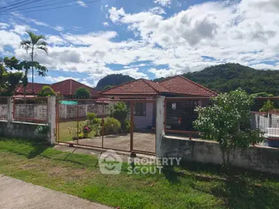 Charming single-story home with red-tiled roof and lush mountain backdrop, perfect for serene living.