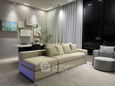 Modern living room with elegant sofa and floor-to-ceiling windows offering stunning night views.