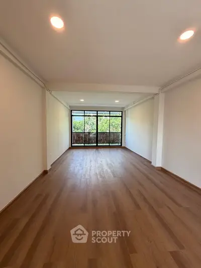 Spacious living room with wooden flooring and large windows offering a serene view.