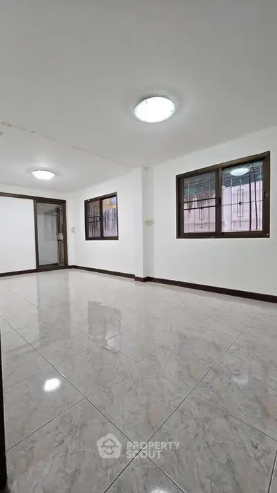 Spacious empty room with tiled flooring and large windows, ideal for customization.