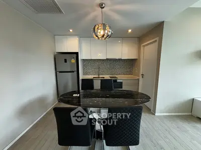 Modern kitchen with sleek black dining table and stylish chairs, featuring contemporary lighting and stainless steel appliances.