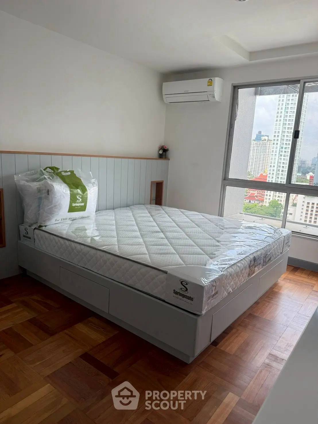 Modern bedroom with city view, featuring a new mattress and air conditioning.