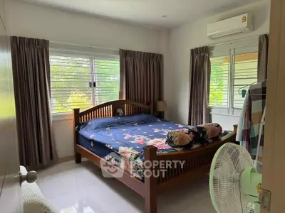 Cozy bedroom with large windows and air conditioning, featuring a wooden bed and floral bedding.