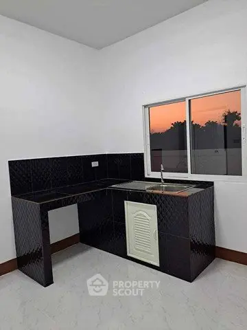 Modern kitchen with sleek black tile countertops and sunset view through window.