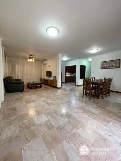 Spacious living room with polished marble flooring, ample lighting, and an open layout leading to a cozy dining area, perfect for entertaining guests.