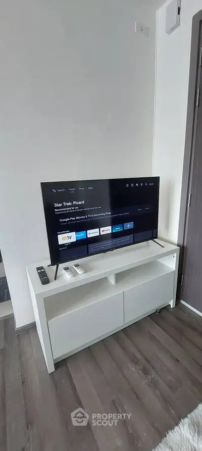 Modern living room with sleek TV setup on white console, featuring wooden flooring and minimalist decor.