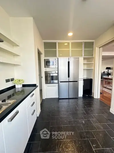 Modern kitchen with sleek appliances and open shelving, featuring a stainless steel fridge and oven.