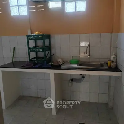 Simple kitchen with tiled walls and open shelving, featuring a sink and basic countertop.