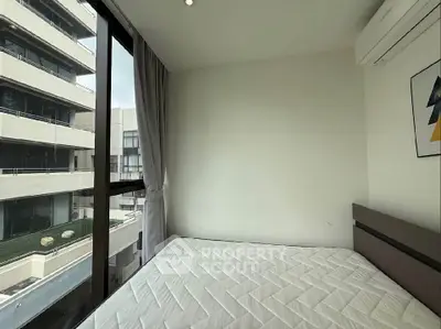 Modern bedroom with large window and city view, featuring minimalist decor and air conditioning.
