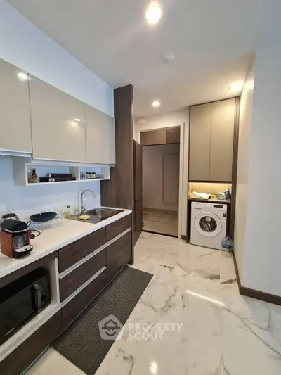 Modern kitchen with sleek cabinets, marble flooring, and built-in washing machine.