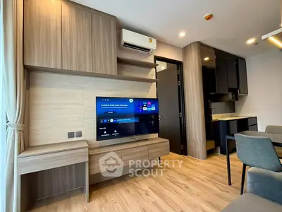 Modern living room with sleek wooden cabinetry and mounted TV, adjacent to a compact kitchen area.