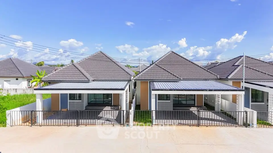Modern twin houses with sleek design and spacious driveways under a clear blue sky.