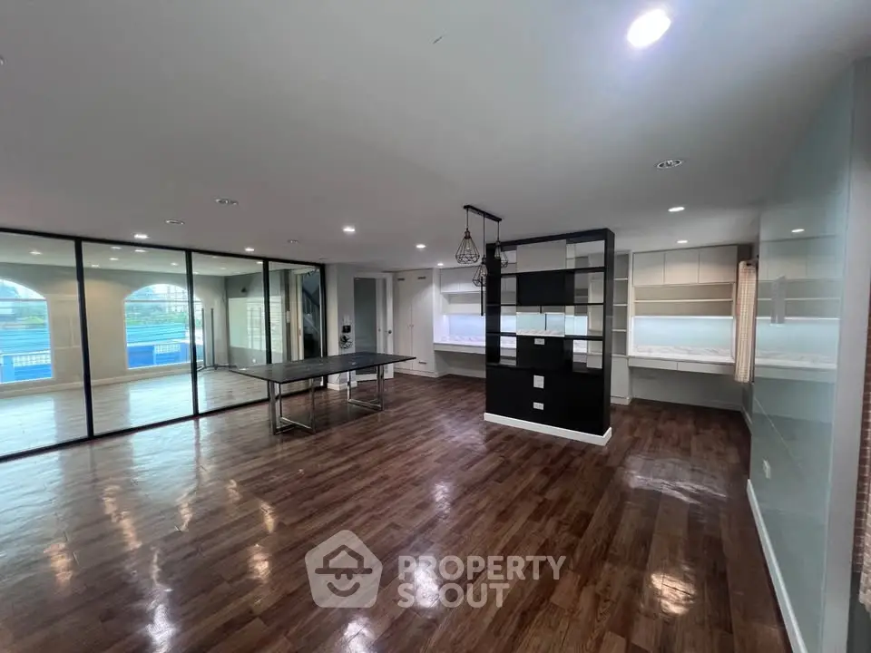 Spacious modern living room with hardwood floors and glass wall overlooking pool area.