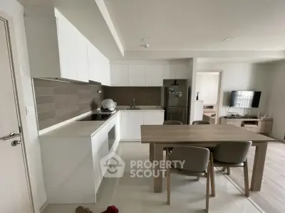 Modern kitchen and dining area with sleek white cabinets and wooden dining table.