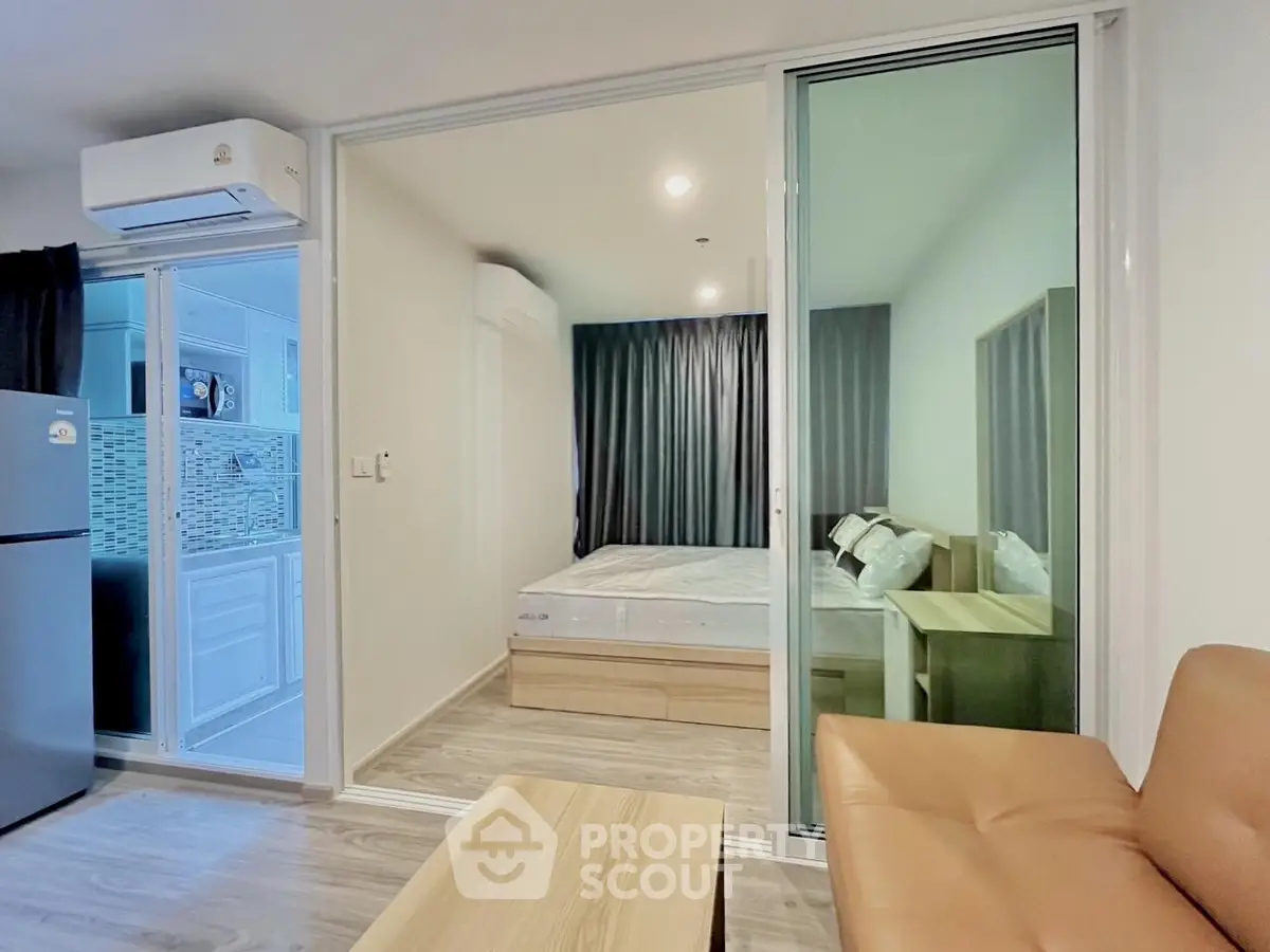 Modern apartment interior with cozy living room and bedroom separated by glass doors.