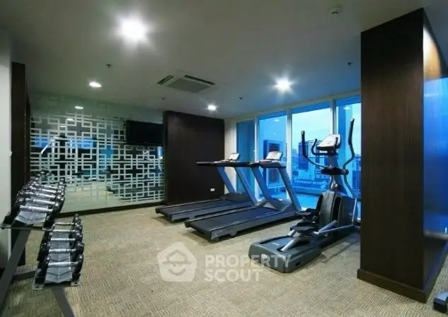 Modern gym with treadmills and weights in a high-rise building with city view.