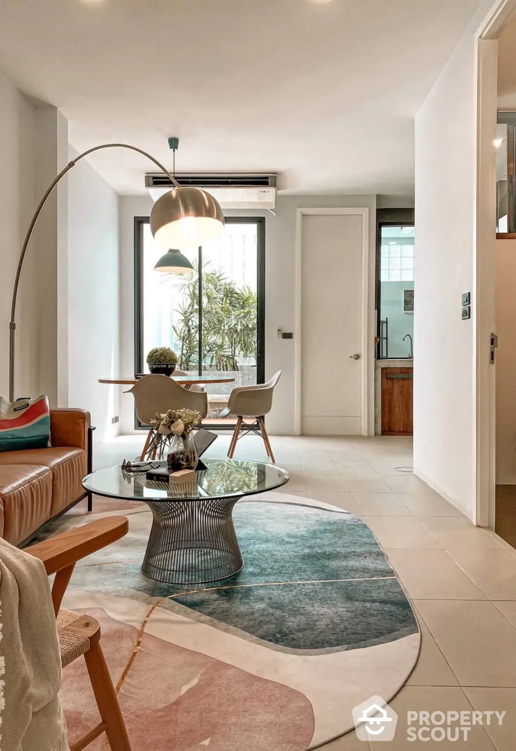 Chic modern living room with elegant furniture and tasteful decor, leading to a sunlit balcony with greenery, showcasing a perfect blend of comfort and style.