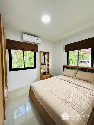 Cozy bedroom with large windows and modern furnishings, offering a serene view of greenery.