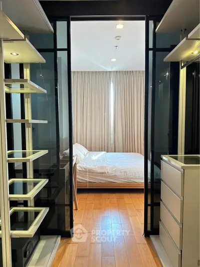 Modern bedroom with sleek glass doors and wooden flooring, featuring a cozy bed and ample storage space.