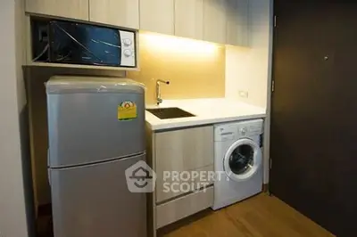 Compact kitchen with modern appliances including fridge, microwave, and washing machine in cozy apartment.