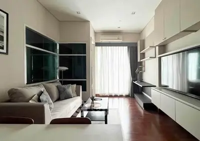 Modern living room with sleek furniture and large TV, featuring natural light from a window.