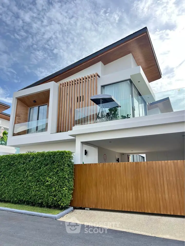 Modern luxury villa with sleek design and lush greenery, featuring large windows and a spacious balcony.
