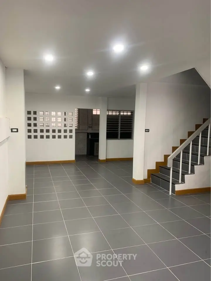 Spacious modern interior with sleek tile flooring and staircase, ideal for customization.
