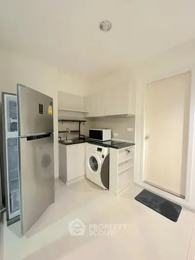 Modern compact kitchen with washing machine and stainless steel fridge in a bright apartment.