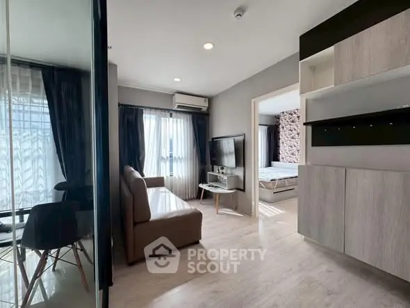 Modern apartment interior with open living room and bedroom, featuring sleek furniture and natural light.